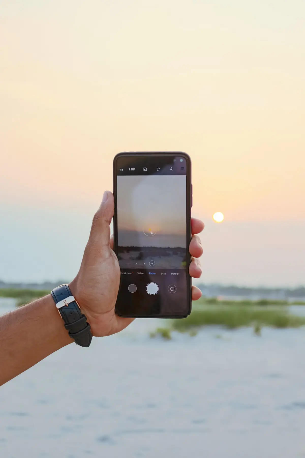 Hand holding a phone at sunset by the sea